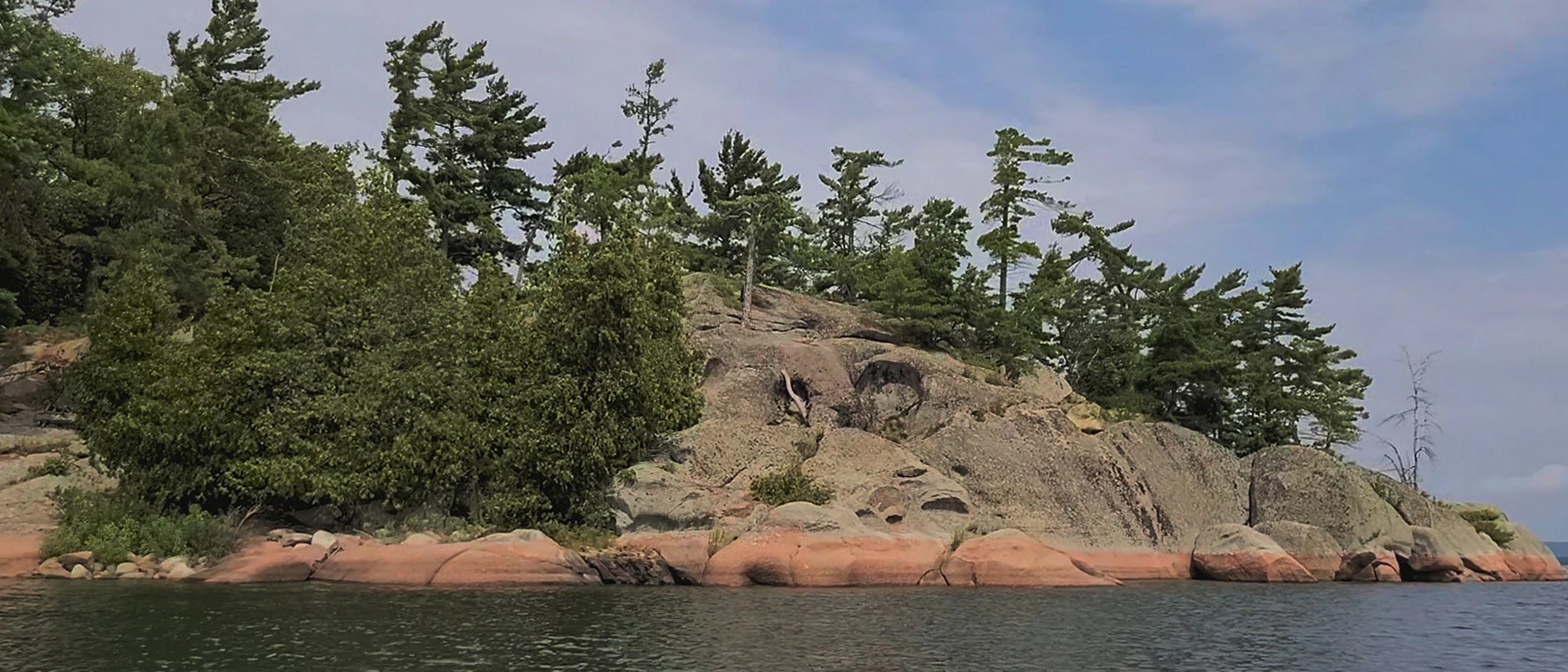 Western Shoreline of the Benjamind islands with red granite rock, white quartzite,
                trees and clear water